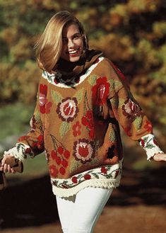 a woman is walking down the street wearing a sweater with flowers on it and a scarf around her neck