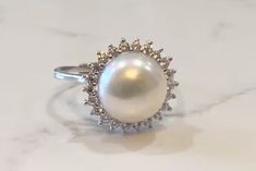 The Pearl is the only gem created in living being. When something penetrates an oyster's shell, it doesn't reject it; it embraces it, encases it & turns it into something beautiful. ♥️ This stunning ring features a freshwater pearl encircled by lustrous crystals. Available in silver or gold. Adjustable, size 5-8 PRODUCT DETAILS: 10mm AAA freshwater button iridescent pearl Luster - High Setting: sterling silver or 14kt gold plated with crystal mount Size: Adjustable, Size 5-8 Materials: Freshwate Timeless White Gold Pearl Ring With Center Stone, Timeless Pearl White Pearl Ring For Anniversary, Timeless Pearl Ring With Prong Setting For Anniversary, White Pearl Ring With Center Stone, Timeless Oval Pearl Ring For Wedding, White Pear Shaped Ring With Center Stone, Timeless Akoya Pearl Round Rings, Timeless Pearl White Ring With Pearl Drop, Timeless Pearl White Rings With Pearl Drop