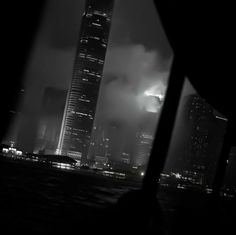 black and white photo of city skyline at night with fog in the air, taken from across the water