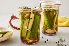 two jars filled with pickles on top of a table next to plates and spoons