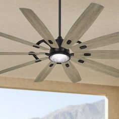 a ceiling fan with five wooden blades and a light on the top is hanging in front of a large window