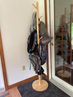 a coat rack with several backpacks hanging on it's sides, in front of a door