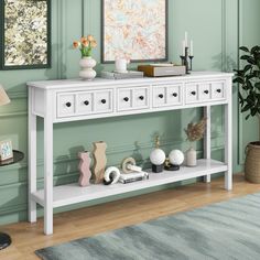 a white console table with three drawers and two candles on it in front of a green wall