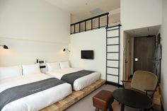 two beds in a hotel room with white and gray bedding, brown chair, and ladder to the ceiling