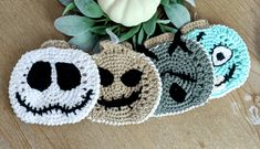 three crocheted coasters with faces on them sitting next to a potted plant