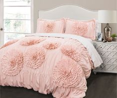 a bed with pink comforters and pillows in a room next to a white dresser