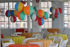 colorful balloons are hanging from the ceiling above tables and chairs in a banquet hall with white linens on them