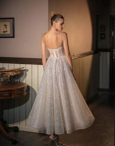 a woman in a white dress is standing near a wall and looking down at the floor