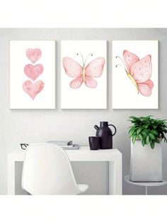 three pink butterfly paintings hanging on the wall next to a white table with a potted plant