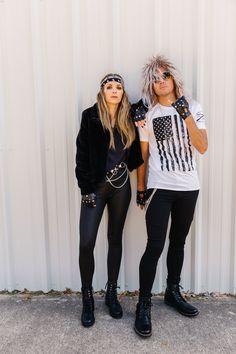 two people standing next to each other in front of a white metal wall wearing punk clothing