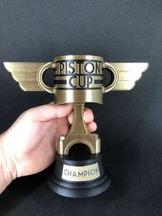 a person holding up a trophy that says piston cup on the front and side of it