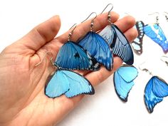 a person is holding some blue butterflies in their hand and four other pieces of jewelry