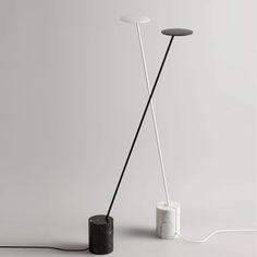 two black and white floor lamps with one light on the other side, in front of a gray wall