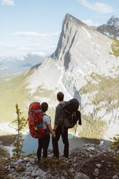 two people with backpacks standing on top of a mountain