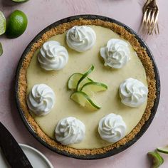 a pie topped with whipped cream and limes on top of a pink table next to utensils