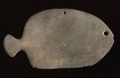 a fish shaped metal object sitting on top of a black surface with holes in it