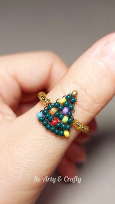 a hand holding a small colorful beaded christmas tree ornament on it's finger