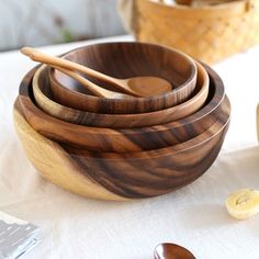 four wooden bowls with spoons in them on a white table cloth next to other wood utensils