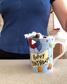 a woman standing in front of a counter holding a cup filled with ice cream and chocolate