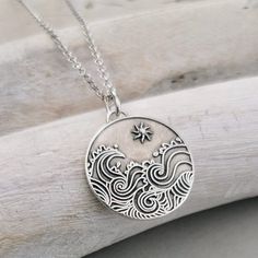 a silver pendant with waves and stars on it sitting on a piece of driftwood