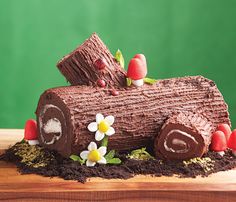 a cake made to look like a log with flowers and leaves around it on a wooden table