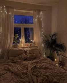 an unmade bed with lights on the windowsill and curtains in front of it