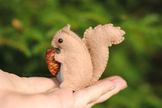 a hand holding a small stuffed squirrel with a pine cone in its mouth