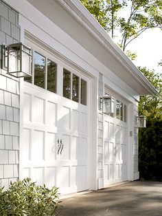 a white garage with two doors and windows on the side of it, next to a bush