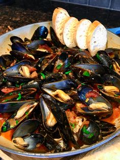 a pan filled with mussels and bread on top of a table