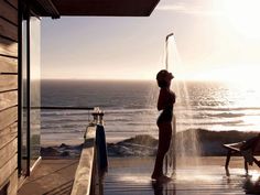 a woman is standing in the water spraying her face with her hands while another person sits on a beach chair