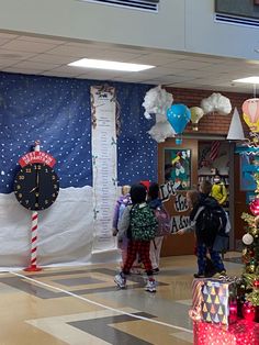 several children are standing in front of a christmas tree with presents on it and balloons hanging from the ceiling