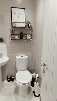 a white toilet sitting in a bathroom next to a sink under a framed art piece