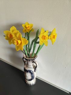 a vase filled with yellow flowers sitting on top of a black table next to a white wall