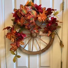 a wreath with fall leaves and ribbons hanging on a door