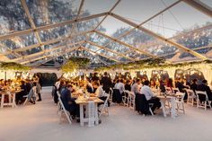 a group of people sitting at tables in a tented area with lights hanging from the ceiling