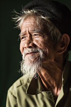 an old man with white hair and a beard wearing a green shirt looking at the camera