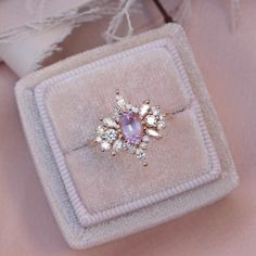 an engagement ring in a velvet box on a pink cloth with white flowers and leaves