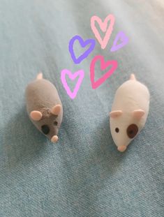 two toy mice sitting next to each other on top of a blue surface with hearts