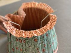 a close up of a paper vase on a table with someone's hand in the background