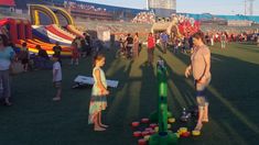 two children are playing with plastic cups on the field at an outdoor game park while people watch