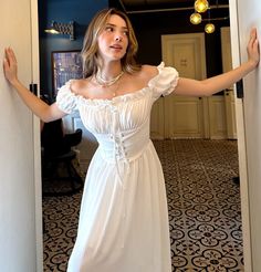 a woman in a white dress is posing for the camera with her hands on the wall