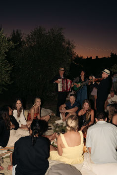 a group of people sitting on top of a field next to each other at night