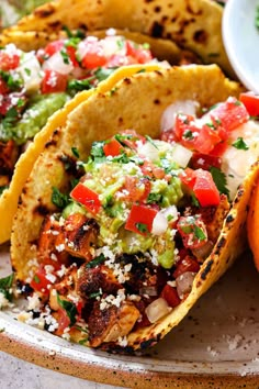 three tacos on a plate with salsa and guacamole in the background