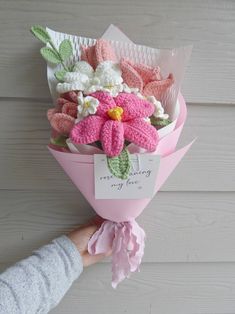 a person holding a bouquet of crocheted flowers in pink and white with a tag on it