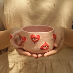 a woman holding a cup with hearts painted on it and eyes drawn on the inside