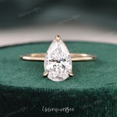 a pear shaped diamond ring sitting on top of a green velvet box