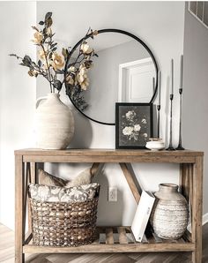 a wooden table topped with vases filled with flowers next to a mirror and framed pictures