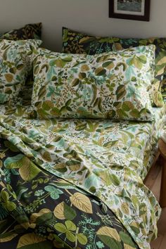 a bed covered in green and yellow floral print sheets with pillows on top of it