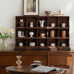 a wooden table topped with lots of cups and saucers next to a vase filled with flowers