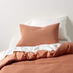 an orange and white bed with two pillows on top of the headboard, next to a light brown comforter